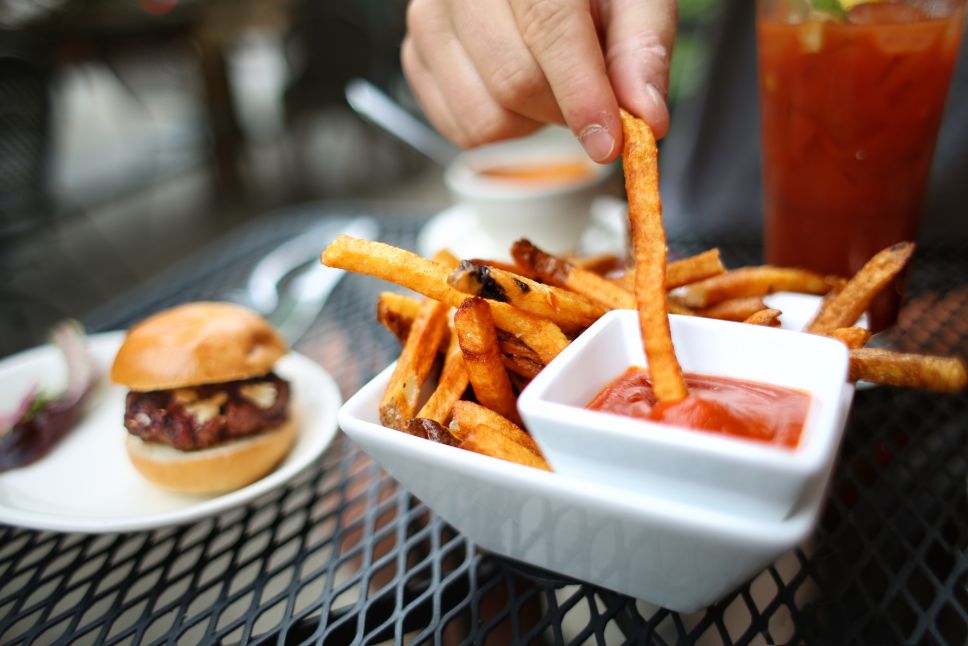 Hand Dipping French Fries in Ketchup with Mini Cheeseburger Sliders