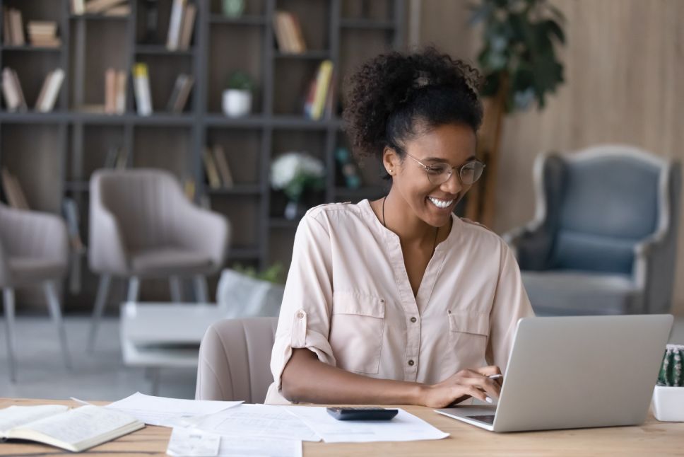 Happy millennial African American woman manage household budget calculate expenses expenditures on machine. Smiling young biracial female pay bills taxes online on computer. Finances concept.