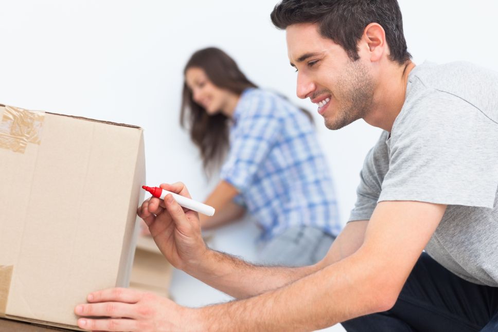 Happy man writing with a red marker on a moving box