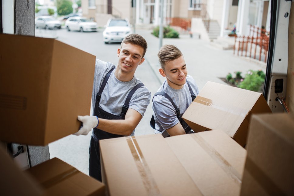 Two young handsome smiling movers wearing uniforms are unloading