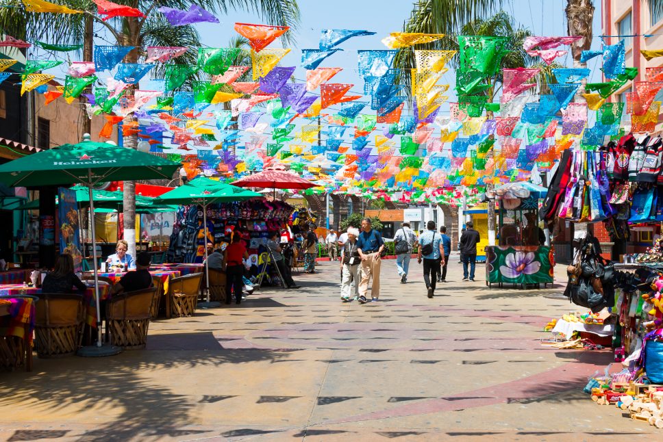 TIJUANA, BAJA CALIFORNIA/MEXICO - JUNE 20, 2018: People shop and dine at Plaza Santa Cecilia, a historic Mexican square with colorful hanging flags.