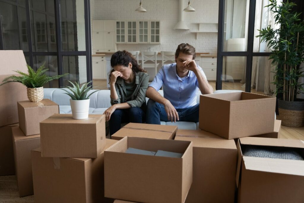 Tired unhappy young Caucasian couple sit on sofa in new living room feel unmotivated unpacking. Upset stressed millennial man and woman have fight quarrel unboxing packages relocating moving.