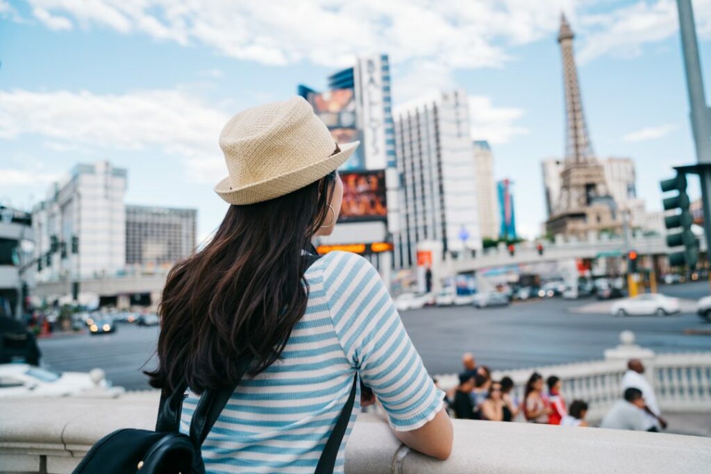 back view of a lady with straw hat watching the tower standing in the busy city. famous tourist attraction in USA. lady backpacker travel alone on spring vacation in Las Vegas.
