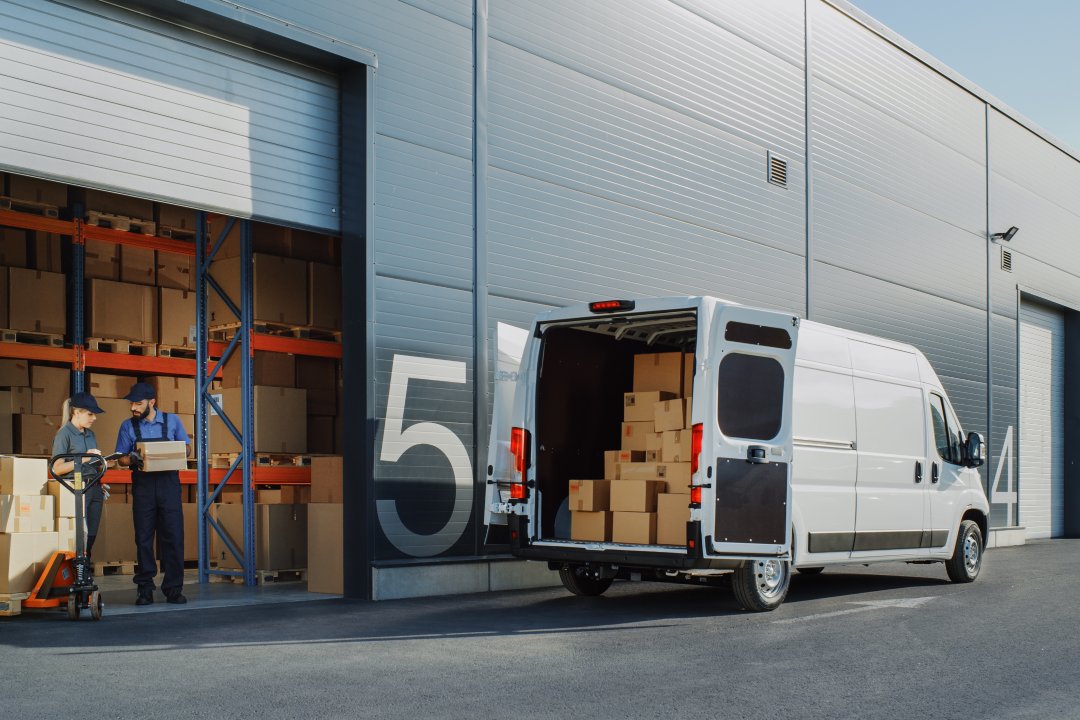 Outside of Logistics Warehouse with Open Door, Delivery Van Loaded with Cardboard Boxes. Truck Delivering Online Orders, Purchases, E-Commerce Goods, Wholesale Merchandise.