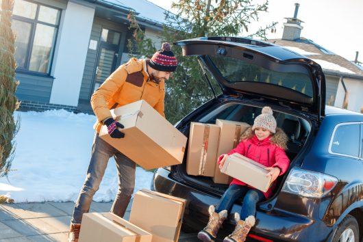 Father and daughter moving to new apartment together during winter standing outdoors near car taking boxes from trunk looking camera smiling excited