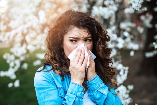 Young woman sneezing in park. Allergy, flu, virus concept.