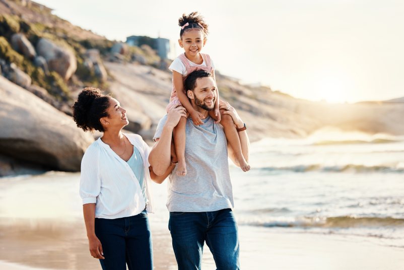 Family on beach, kid on father shoulders and travel with bonding, love and walking together in nature. Vacation, ocean and happy people outdoor, parents and kid with sunshine and adventure with fun