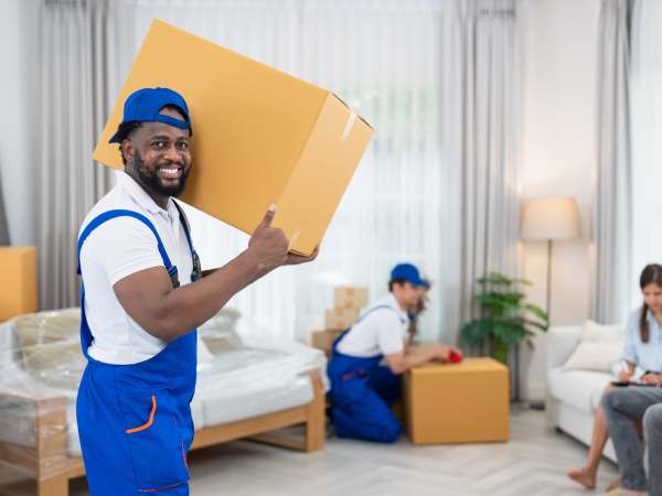 Smiling man mover worker in blue uniform carrying cardboard boxes moving to living room in new house.Professional delivery and moving service.