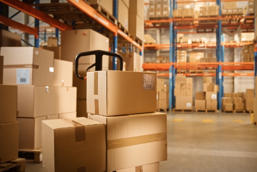 Big Retail Warehouse full of Shelves with Goods Stored on Manual Pallet Truck in Cardboard Boxes and Packages. Forklift Driving in Background. Logistics and Distribution Facility for Product Delivery