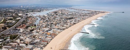 Aerial View of Newport Beach, California, Showing a Sandy Shoreline with Waves Crashing Incessantly into the Partially Submerged Jetties