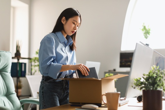 Asian Employee Woman Packing Belongings In Cardboard Box Leaving Workplace Standing In Modern Office Indoor. Staff Reduction, Unemployment Problem Concept
