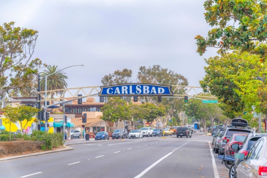 CARLSBAD, CALIFORNIA - CIRCA FEB 2021: Welcome sign over the highway at downtown city. Welcome sign at the instersection road with road side parking spaces.