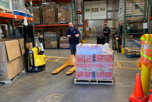 A man stands in a warehouse surrounded by stacked boxes and pallets, showcasing business storage options in San Marcos.
