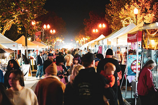 A bustling crowd navigates a vibrant night market, illuminated by colorful lights in Murrieta, CA.
