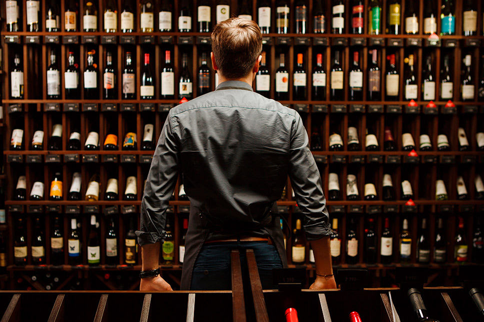 A man poses by a wine rack, highlighting his wine collection as he prepares to move in Southern California.