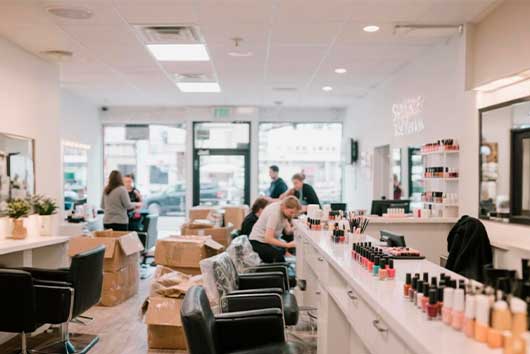 Inside a salon, people are seated at the counter while boxes are placed on the floor, suggesting an upcoming move.