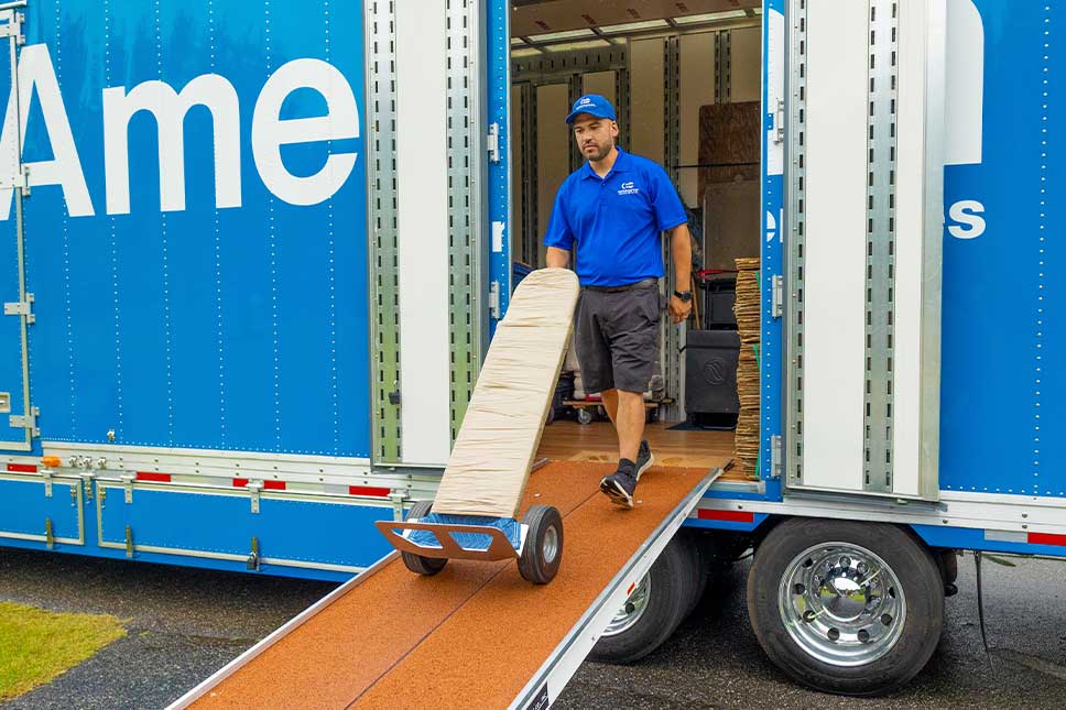 A man is seen loading a moving truck with a ramp, focused on securing heavy items for transport.