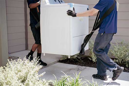 Two men transporting a washing machine outdoors, showcasing proper technique for handling heavy items.